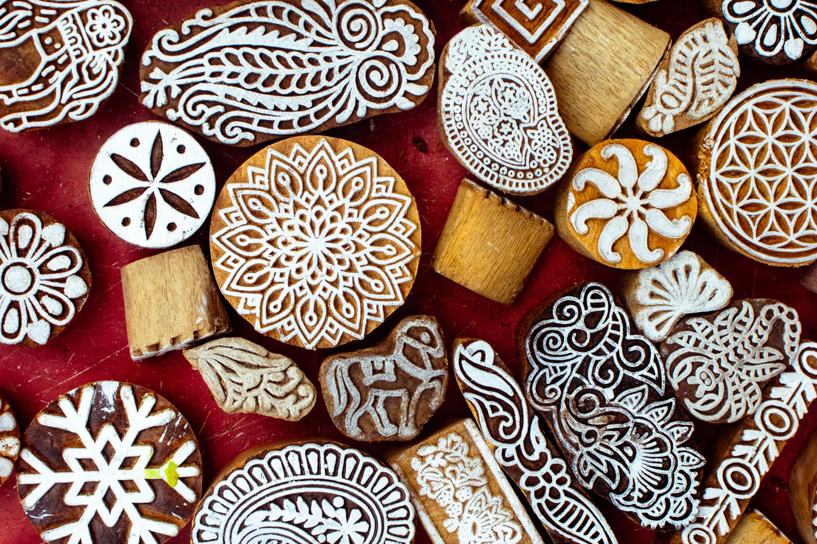 Hand-carved wooden printing blocks with intricate floral and paisley patterns laid out on a red surface