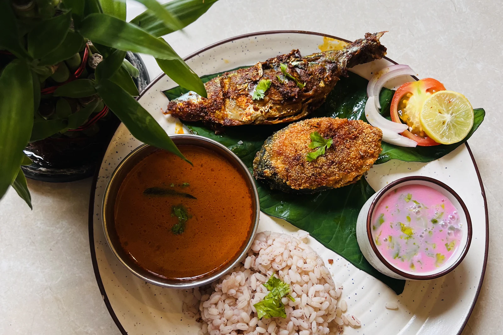 A Goan fish thali: fried mackerel and rava-crusted fish on a banana leaf, a bowl of coconut fish curry, red parboiled rice and a glass of pink kokum solkadhi